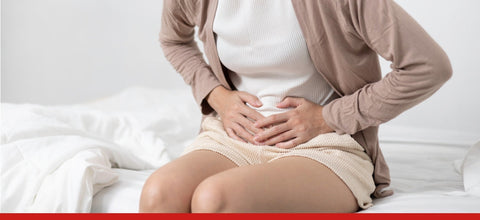 Donna con dolore addominale, mani sullo stomaco, su letto bianco.