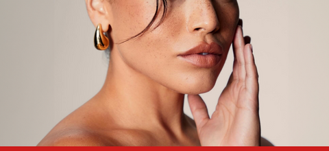 Donna con lentiggini e pelle luminosa, tocca delicatamente il viso, simbolo di benessere naturale.
