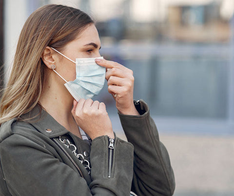 Donna bionda con giacca verde che indossa una mascherina protettiva, simbolo di prevenzione e benessere.