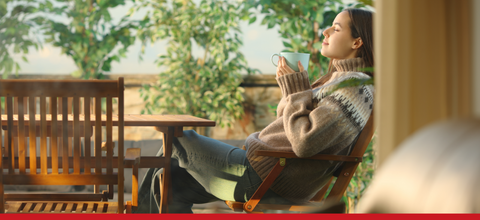 Donna rilassata con tazza di tè, godendosi il sole all'aperto, simbolo di benessere naturale e relax.