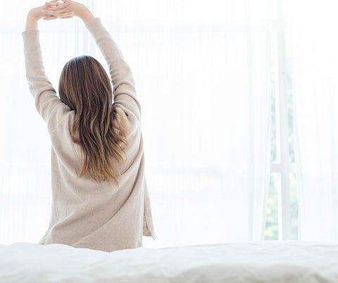Donna si stira al mattino con luce naturale, simbolo di benessere e vitalità.