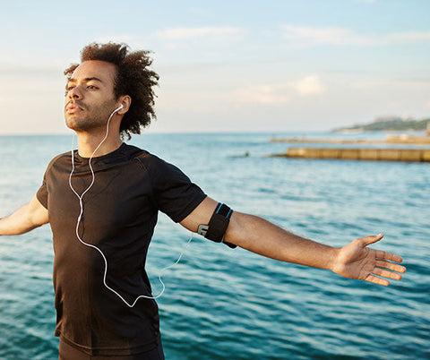 Uomo con cuffie che respira profondamente all'aperto, vicino al mare, per benessere naturale.