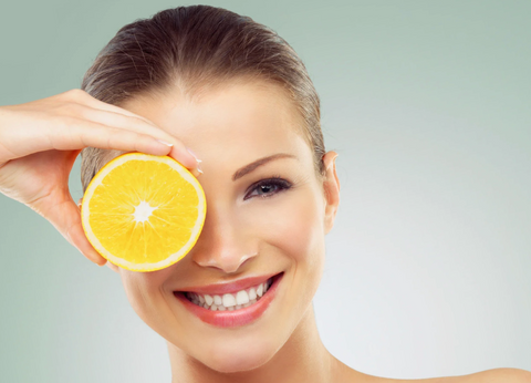Donna sorridente con fetta d'arancia sull'occhio, simbolo di benessere naturale e ingredienti bioattivi.